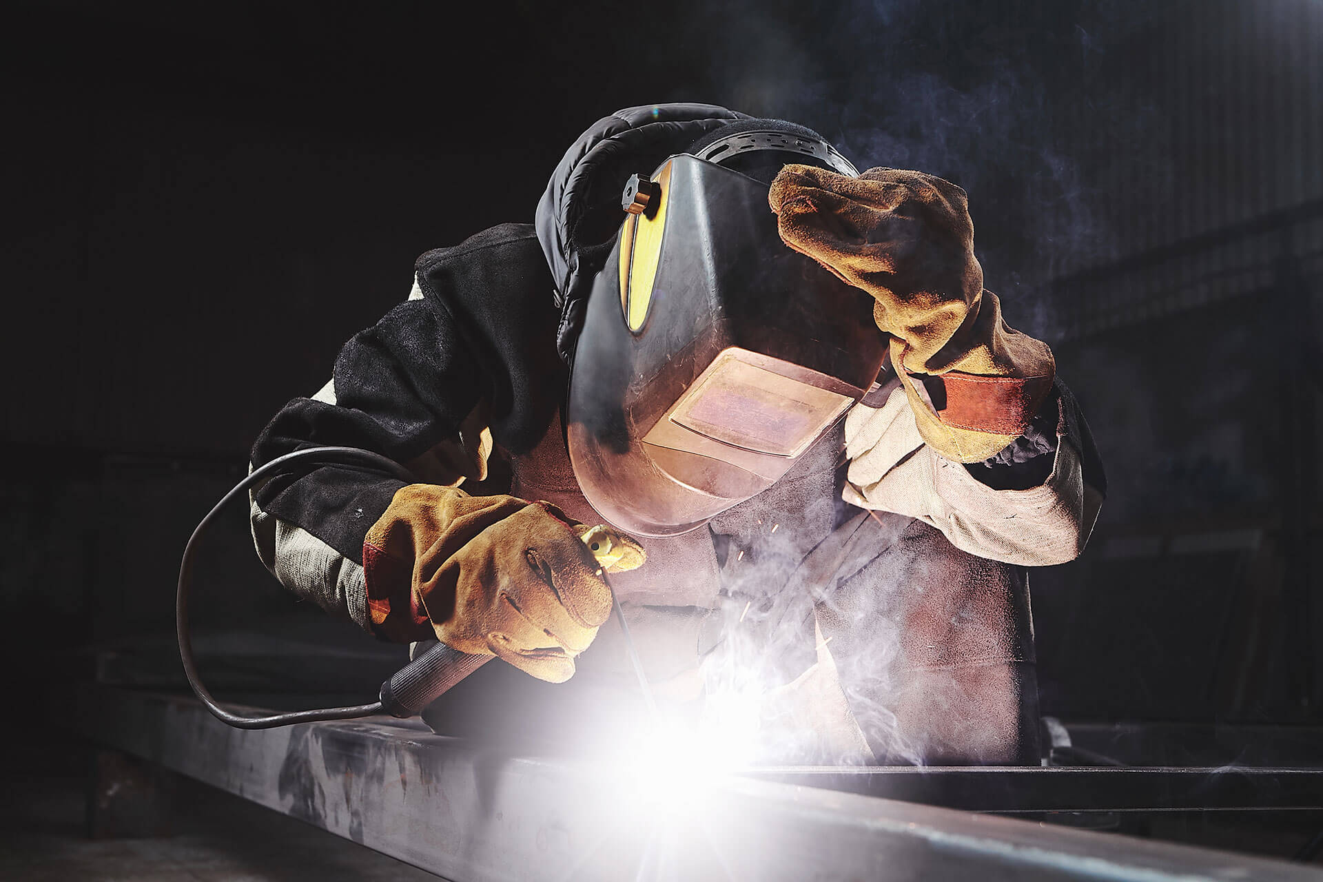 Welder in a protective mask arc-welding a steel beam, bright arc and smoke